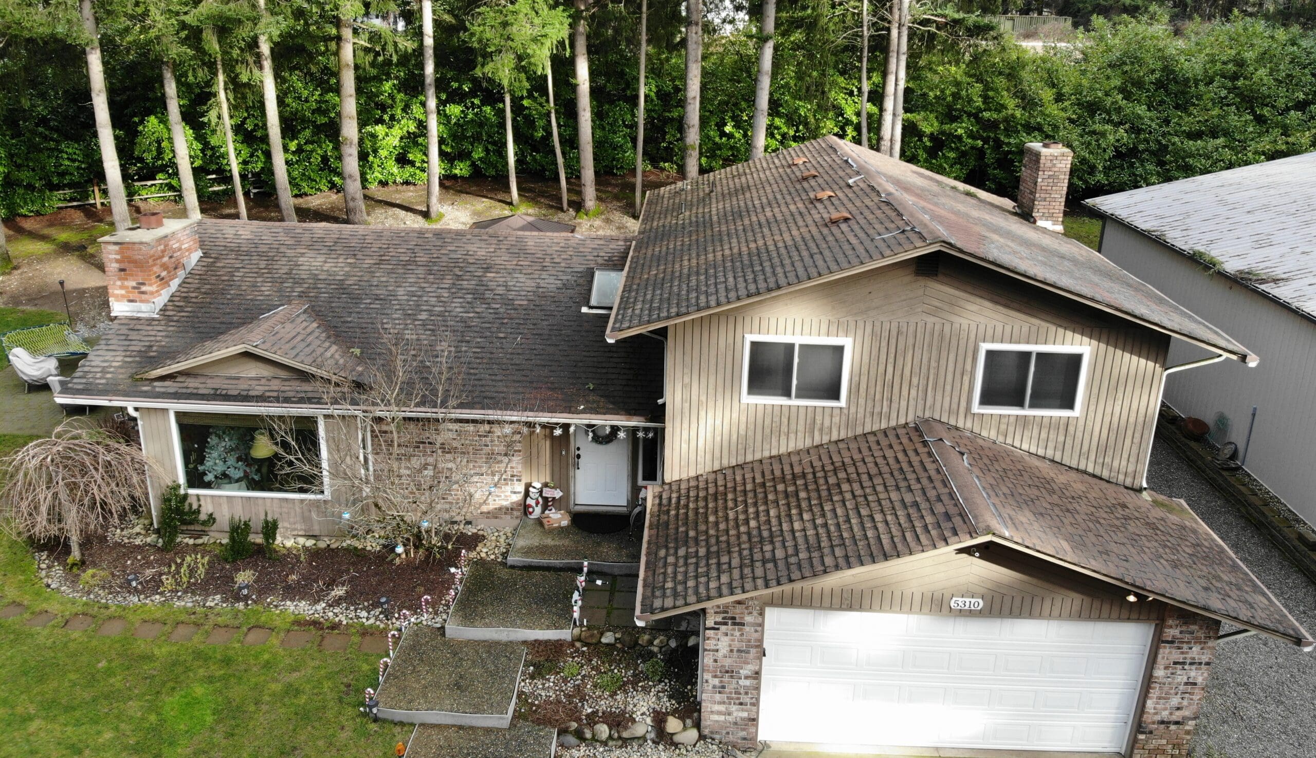 A home with an as-halt shingle roof that looks worn with large trees in the backyard to help illustrate metal roof vs asphalt shingles