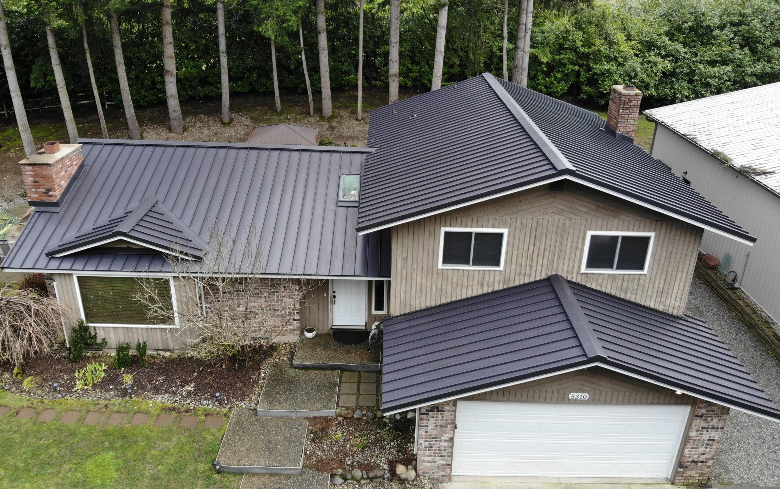 A new standing seam metal roof on a home with large trees in the backyard to help illustrate metal roof vs asphalt shingles